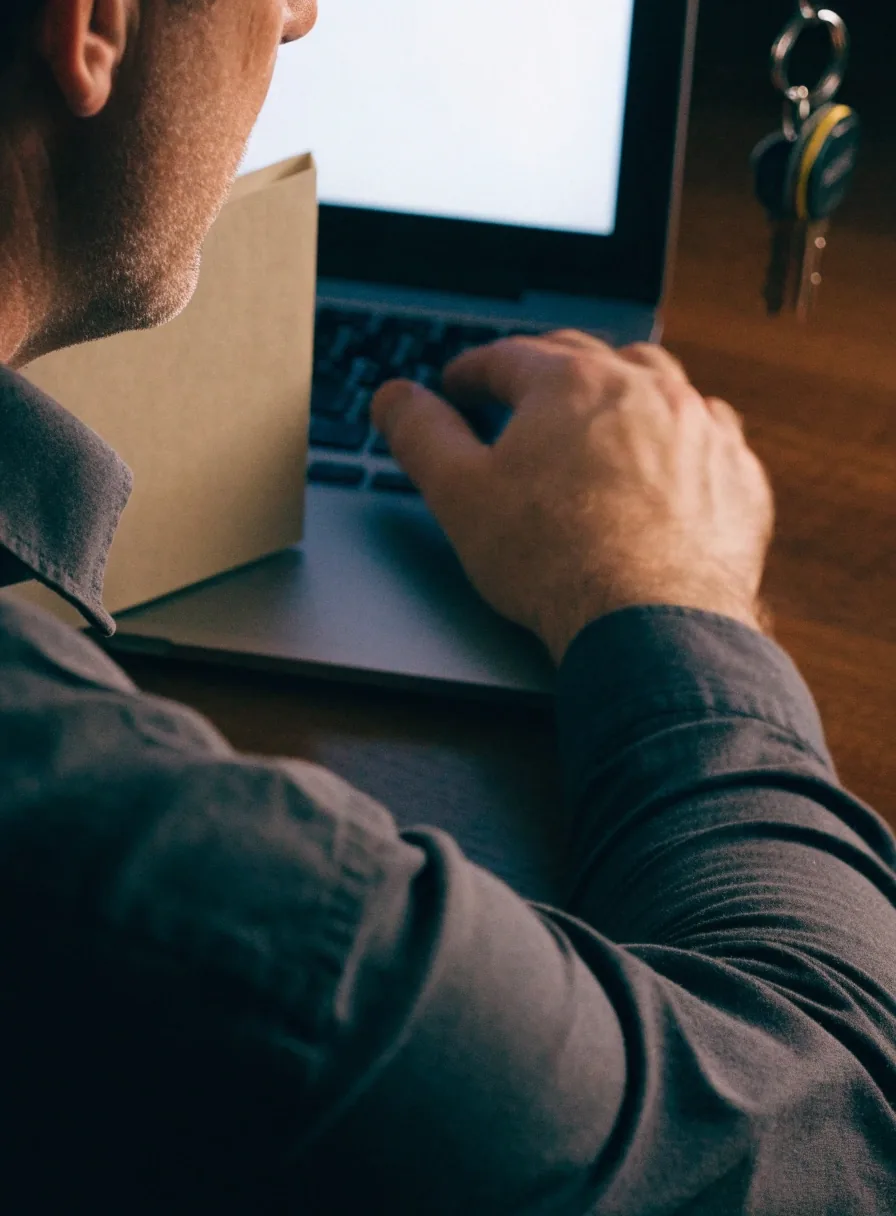 Driver reviewing browser privacy settings on a laptop at a home desk, car keys and a registration folder beside it